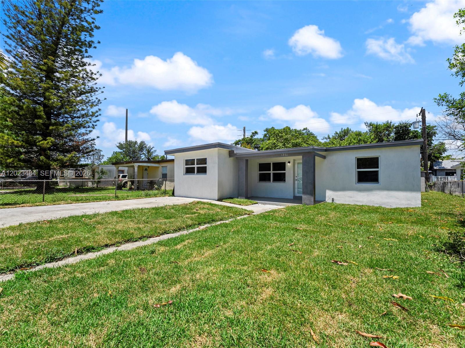 A single-story white house with a flat roof and a front lawn under a blue sky — 1961 Rutland St, Opa-Locka FL 33054, OPA-LOCKA, FL
