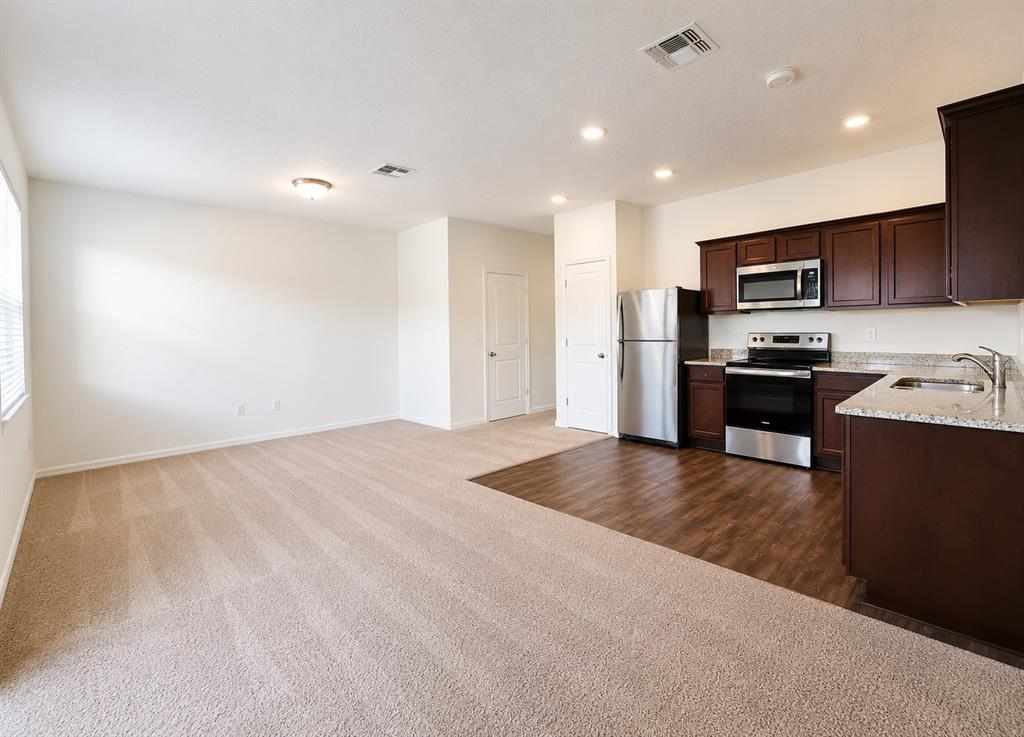 An open-concept kitchen with dark wood cabinets and stainless steel appliances overlooks a carpeted living area — 936 GRANDIN STREET, DAVENPORT, FL