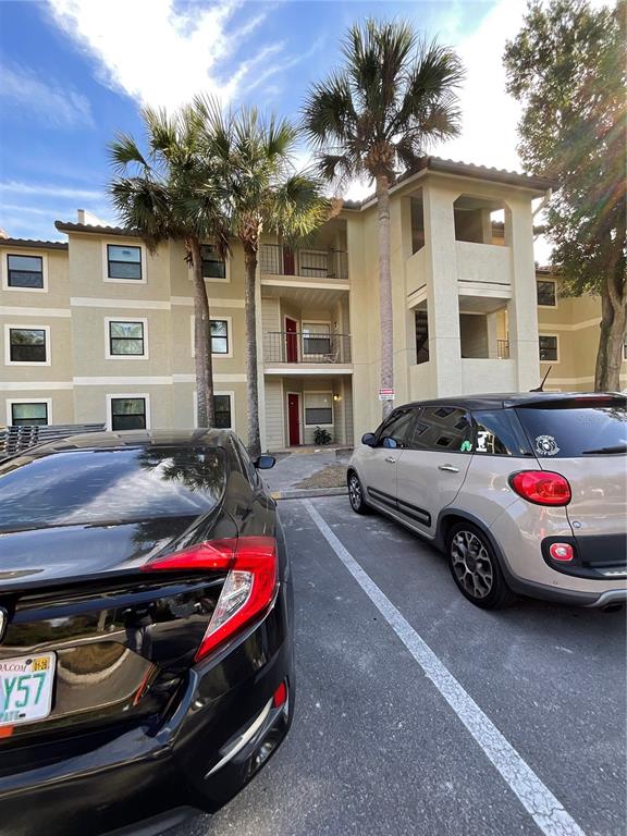 A three-story apartment building exterior features tan stucco walls, palm trees, and parked cars — 3028 PARKWAY BOULEVARD UNIT 105, KISSIMMEE, FL