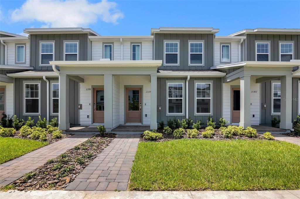 A row of modern two-story townhouses features gray siding, white trim, and individual front entrances — 11390 NONA SOUND STREET, ORLANDO, FL