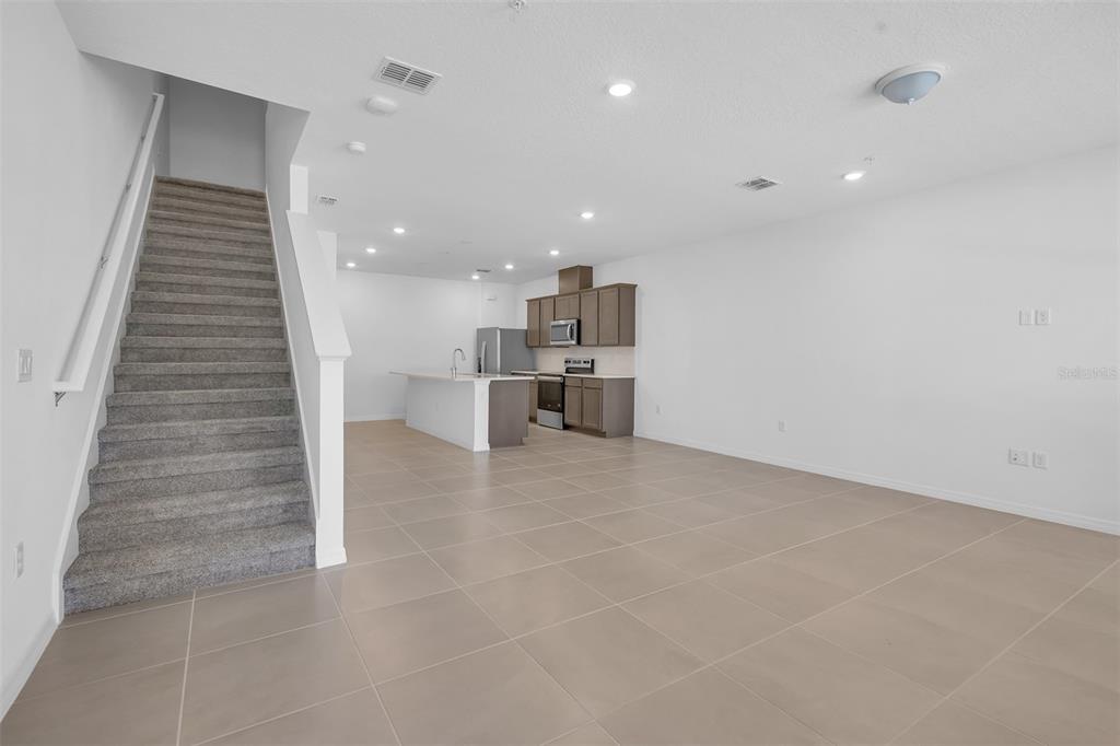 An open-concept living area features a carpeted staircase, tile flooring, and a modern kitchen — 11390 NONA SOUND STREET, ORLANDO, FL