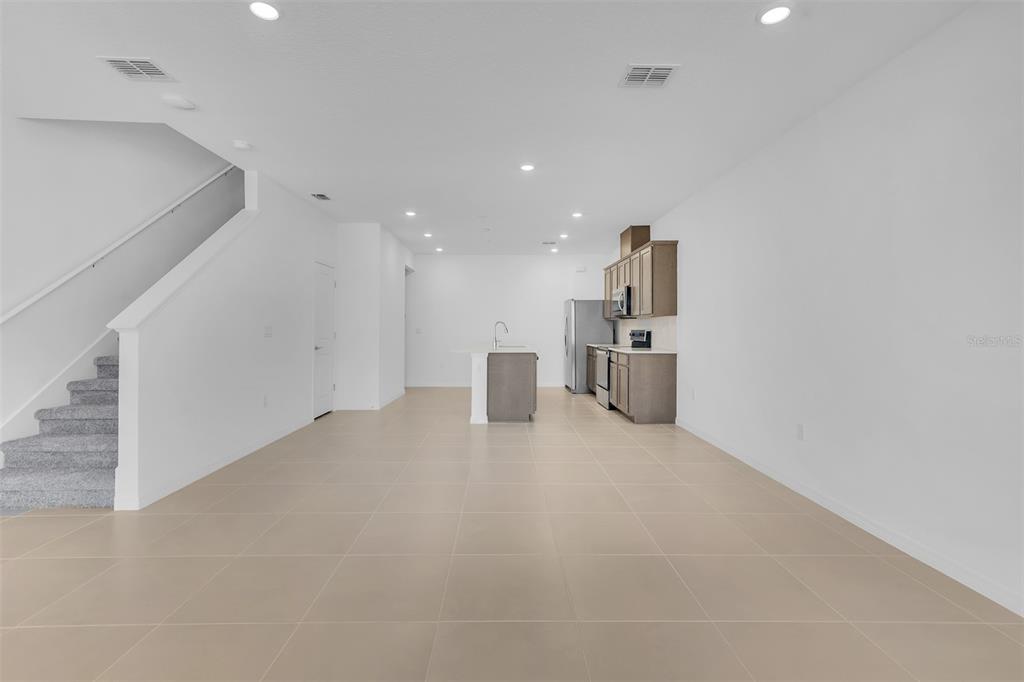 An open-concept kitchen and living area features light tile flooring and a carpeted staircase — 11390 NONA SOUND STREET, ORLANDO, FL