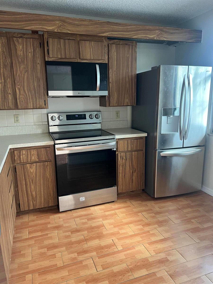 A kitchen features wood-grain cabinets, stainless steel appliances, and light-colored tile flooring — 3540 Whitehall Drive # 203, West Palm Beach FL 33401, WEST PALM BEACH, FL