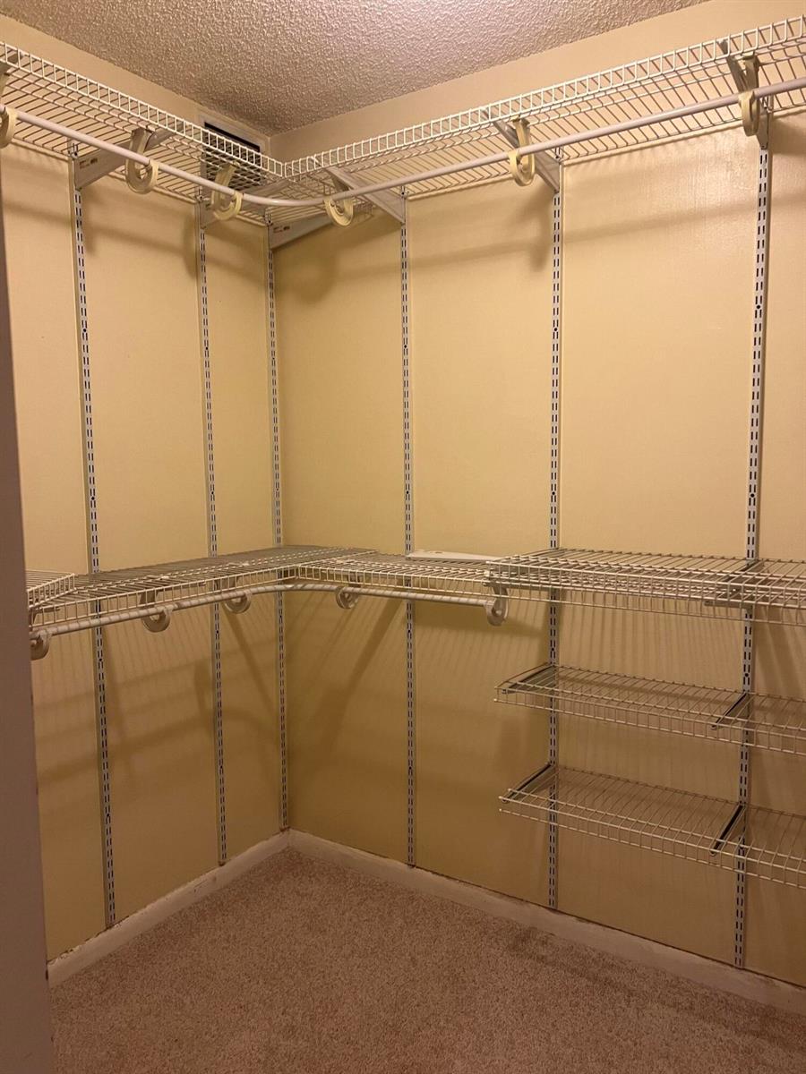 A walk-in closet features white wire shelving units mounted on beige walls over carpeted flooring — 3540 Whitehall Drive # 203, West Palm Beach FL 33401, WEST PALM BEACH, FL