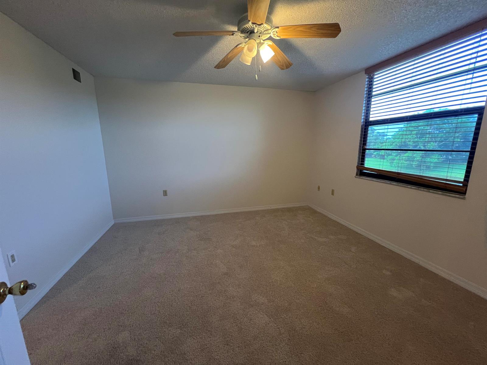 An empty bedroom features beige carpet, white walls, a ceiling fan, and a window with blinds — 3540 Whitehall Drive # 203, West Palm Beach FL 33401, WEST PALM BEACH, FL