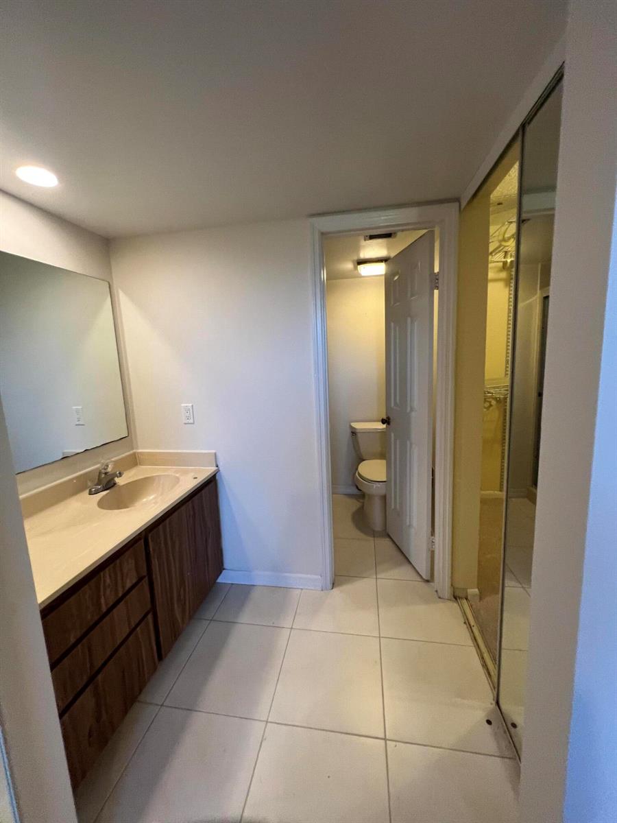 A bathroom features a wood vanity, a mirror, tiled floors, and a separate toilet room — 3540 Whitehall Drive # 203, West Palm Beach FL 33401, WEST PALM BEACH, FL