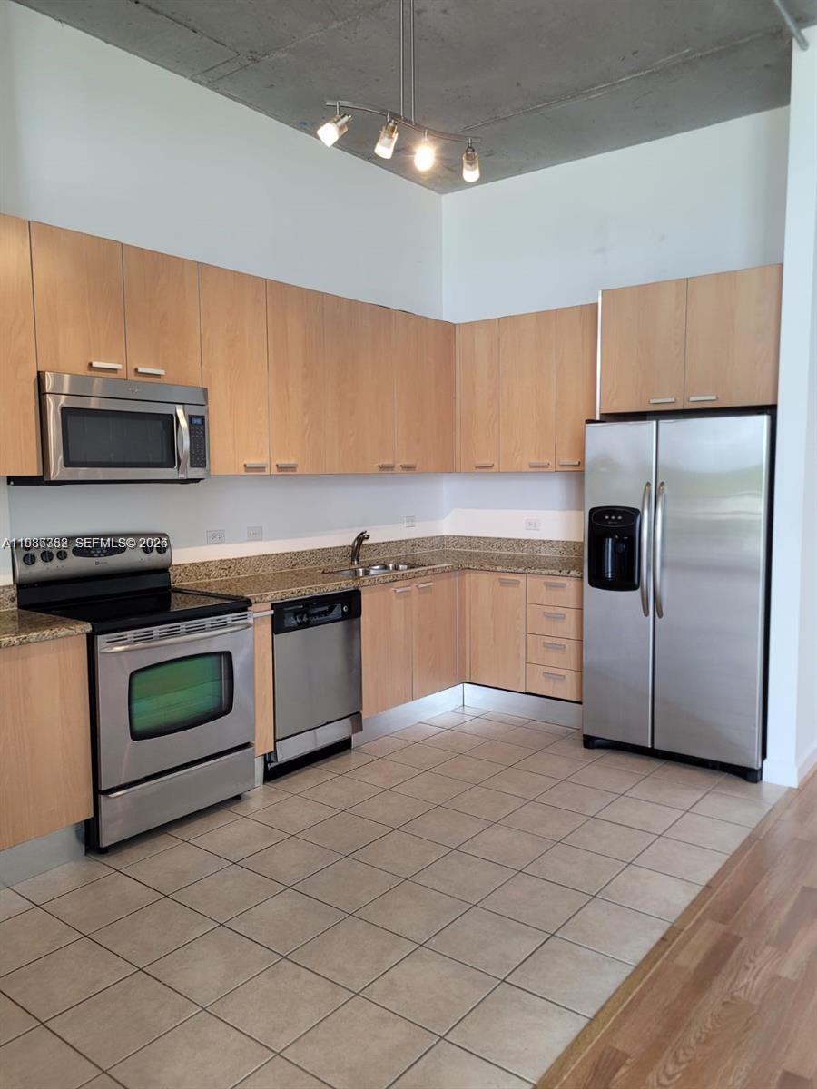 A kitchen features light wood cabinets, stainless steel appliances, granite countertops, and a concrete ceiling — 2100 Van Buren St # 501, Hollywood FL 33020, HOLLYWOOD, FL