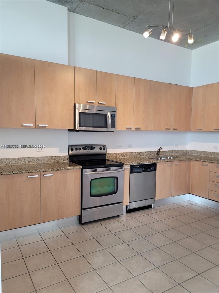 A kitchen features light wood cabinets, stainless steel appliances, granite countertops, and tile flooring — 2100 Van Buren St # 501, Hollywood FL 33020, HOLLYWOOD, FL