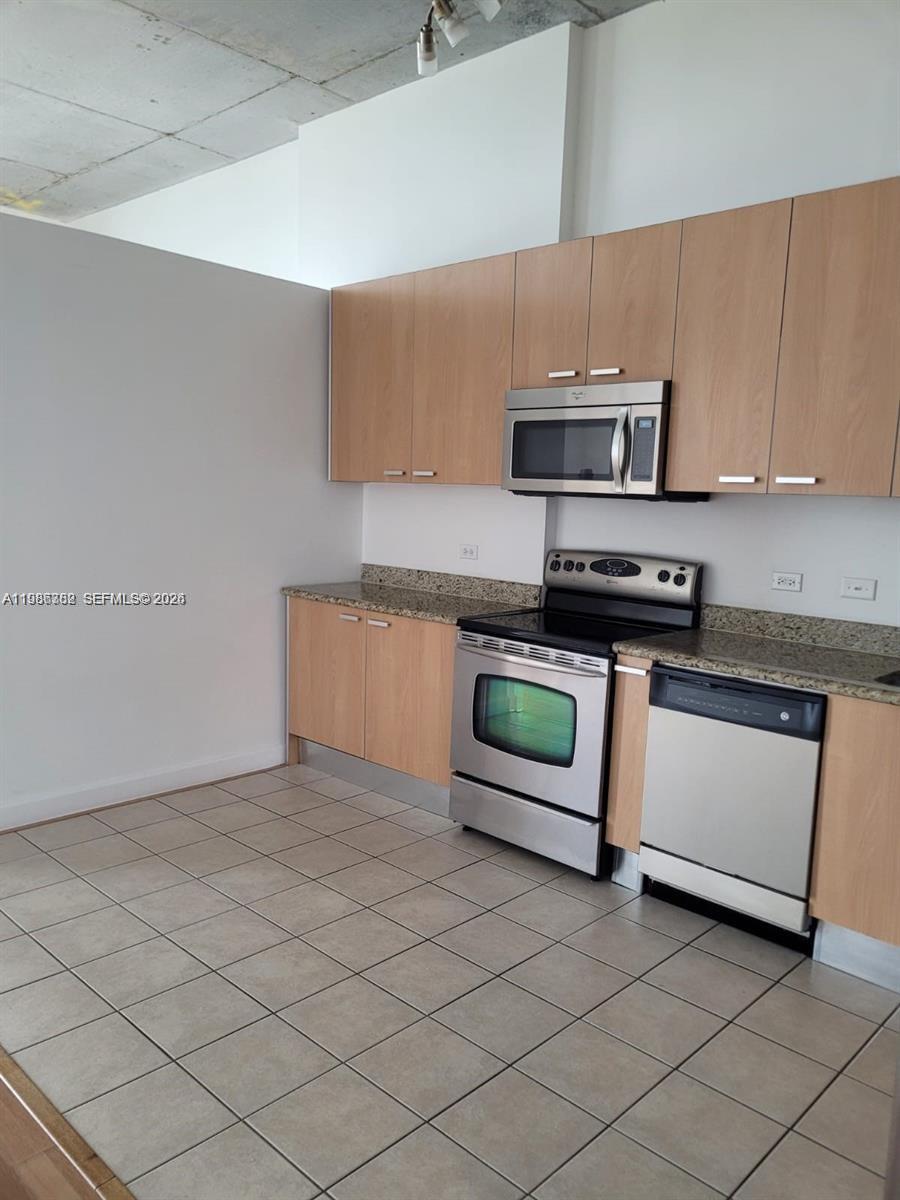 A kitchen features light wood cabinets, stainless steel appliances, and tan tile flooring — 2100 Van Buren St # 501, Hollywood FL 33020, HOLLYWOOD, FL