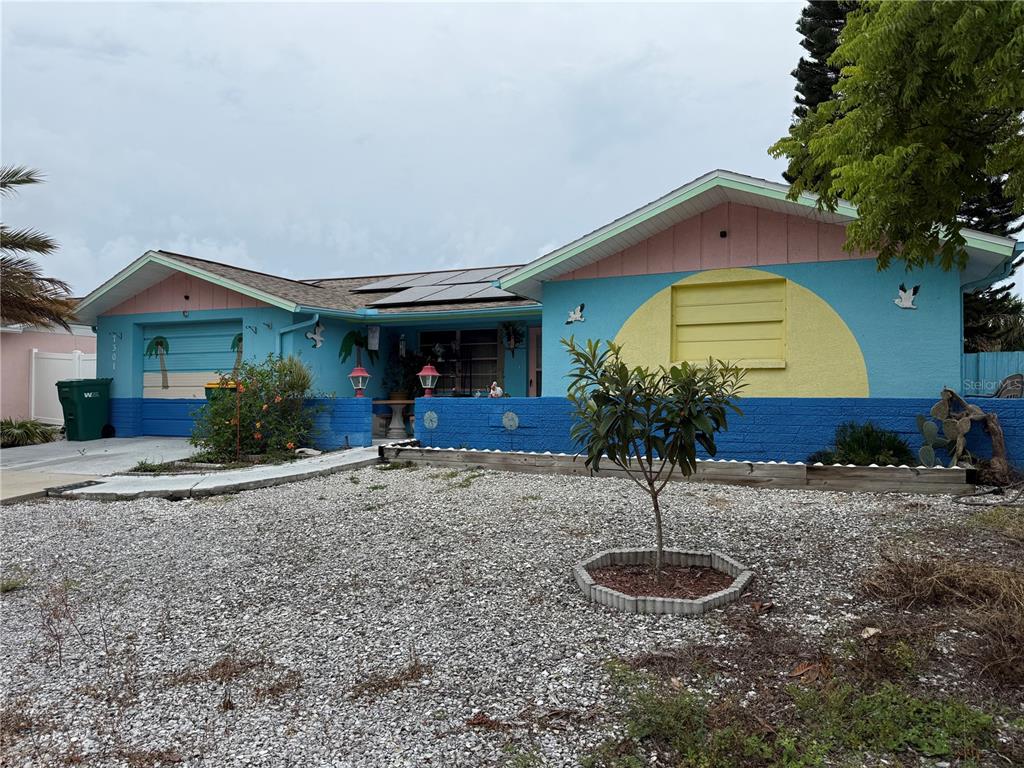 A single-story house with a blue, pink, and yellow exterior and a gravel front yard — 7301 SAN CARLOS DRIVE, PORT RICHEY, FL