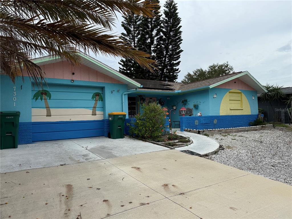 A single-story house with a blue and pink exterior, painted palm trees, and a concrete driveway — 7301 SAN CARLOS DRIVE, PORT RICHEY, FL