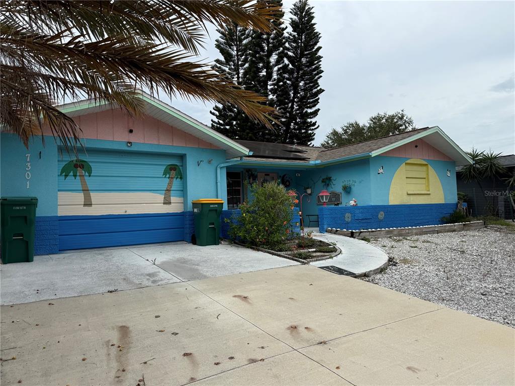 A single-story house features a blue exterior with a painted palm tree garage door — 7301 SAN CARLOS DRIVE, PORT RICHEY, FL