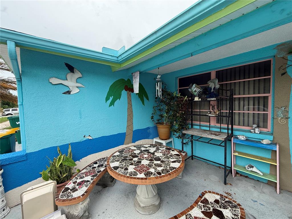 A patio features a mosaic-tiled table and benches against a blue wall with painted murals — 7301 SAN CARLOS DRIVE, PORT RICHEY, FL