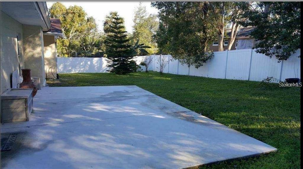 A concrete patio extends from the side of a house into a fenced grassy backyard — 637 PEACHWOOD DRIVE, ALTAMONTE SPRINGS, FL