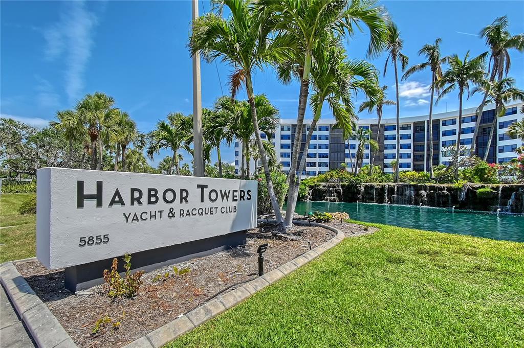 A sign for Harbor Towers Yacht & Racquet Club stands before a pond and building — 5855 MIDNIGHT PASS ROAD UNIT 510, SARASOTA, FL