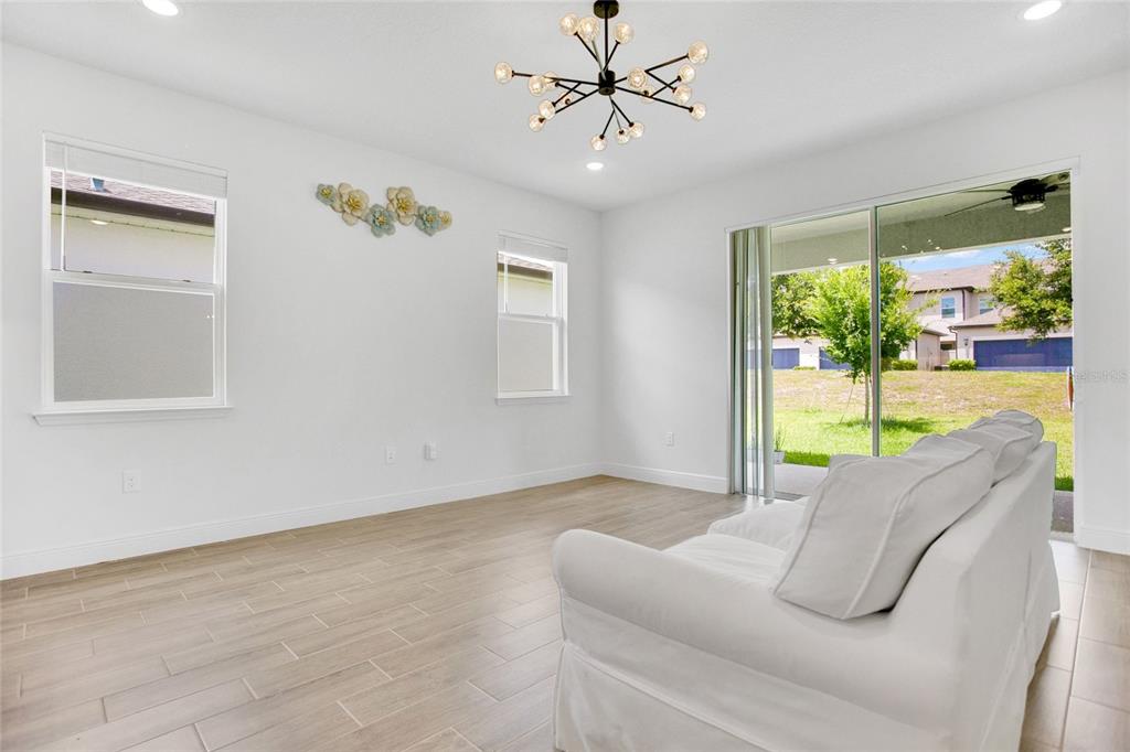 A bright living room features white walls, wood-look tile flooring, a modern chandelier, and sliding doors — 9481 EMERALD BERRY DRIVE, WINTER GARDEN, FL