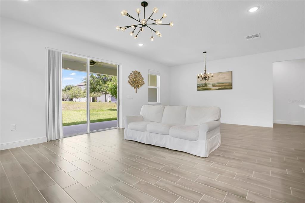 A living room with light wood-look tile floors, a white sofa, and two light fixtures — 9481 EMERALD BERRY DRIVE, WINTER GARDEN, FL