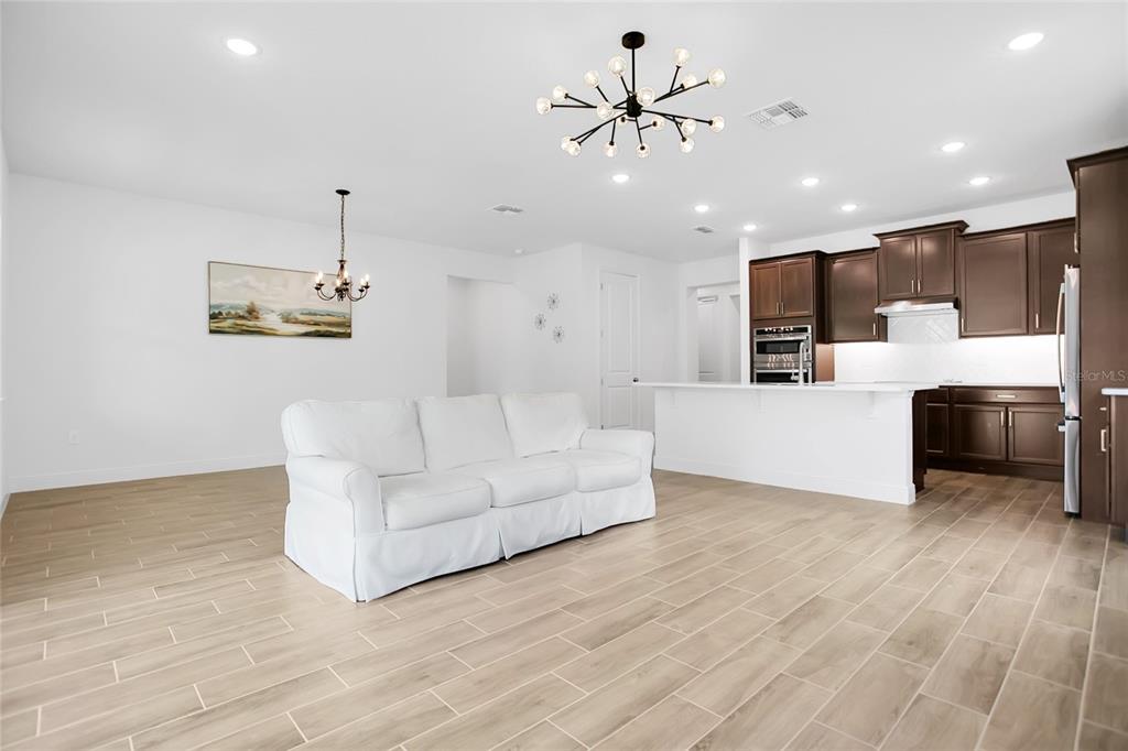 An open-concept living room and kitchen featuring white walls, light tile flooring, and dark cabinetry — 9481 EMERALD BERRY DRIVE, WINTER GARDEN, FL