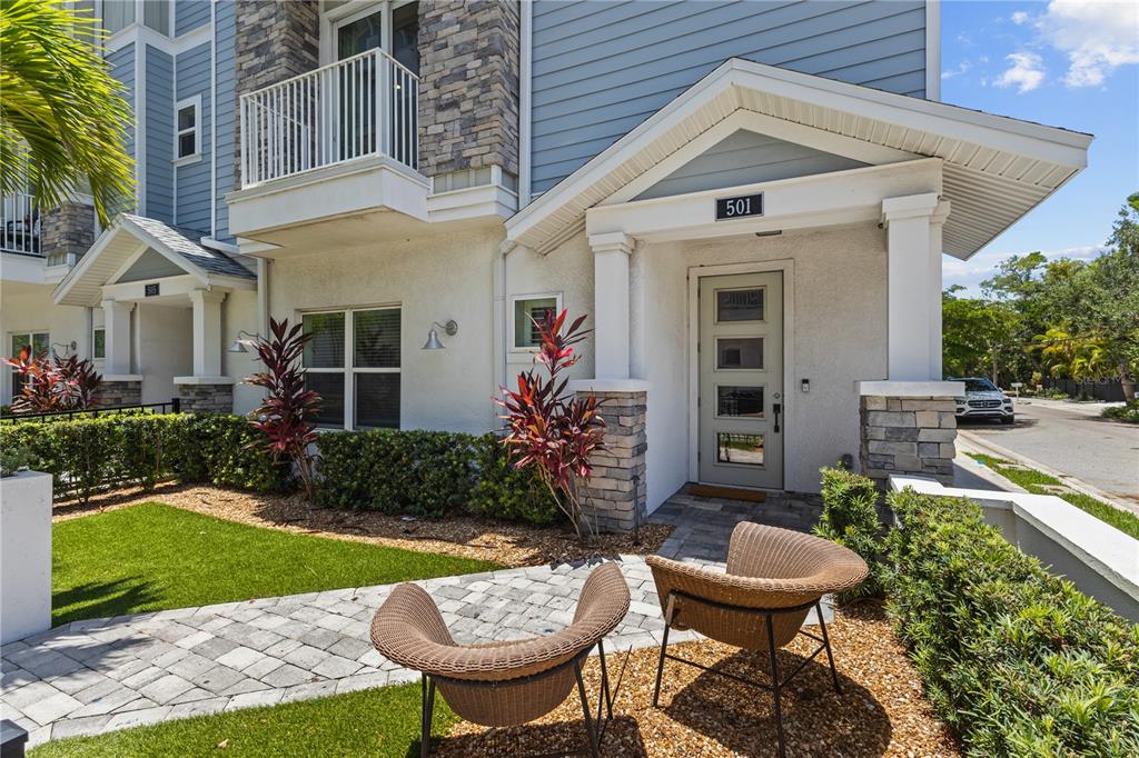 The exterior of a multi-story townhouse features a stone-accented entryway, a paved walkway, and chairs — 501 LAFAYETTE COURT, SARASOTA, FL