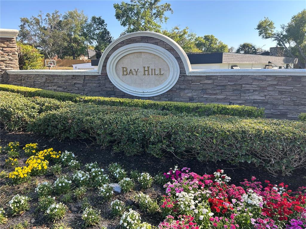 A stone wall with a Bay Hill sign sits behind a garden of colorful flowers — 5701 TARAWOOD DRIVE, ORLANDO, FL