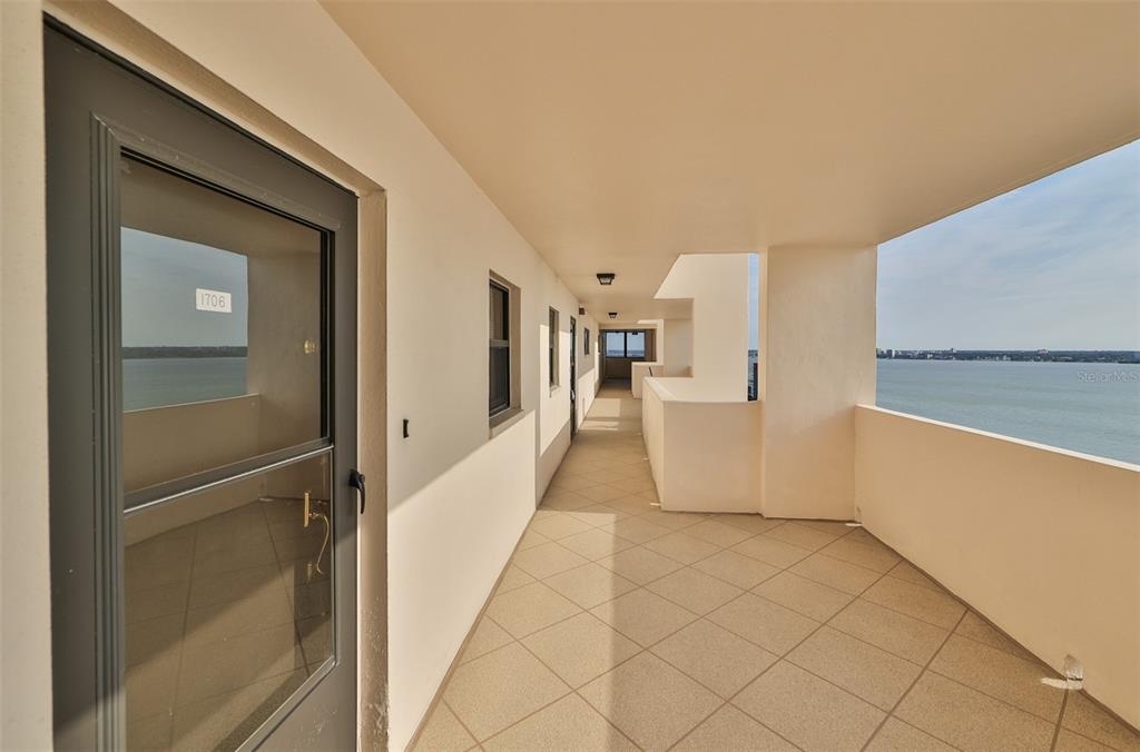 An outdoor apartment hallway features tiled flooring, a gray door, and a view of water — 1270 GULF BOULEVARD UNIT 1706, CLEARWATER BEACH, FL