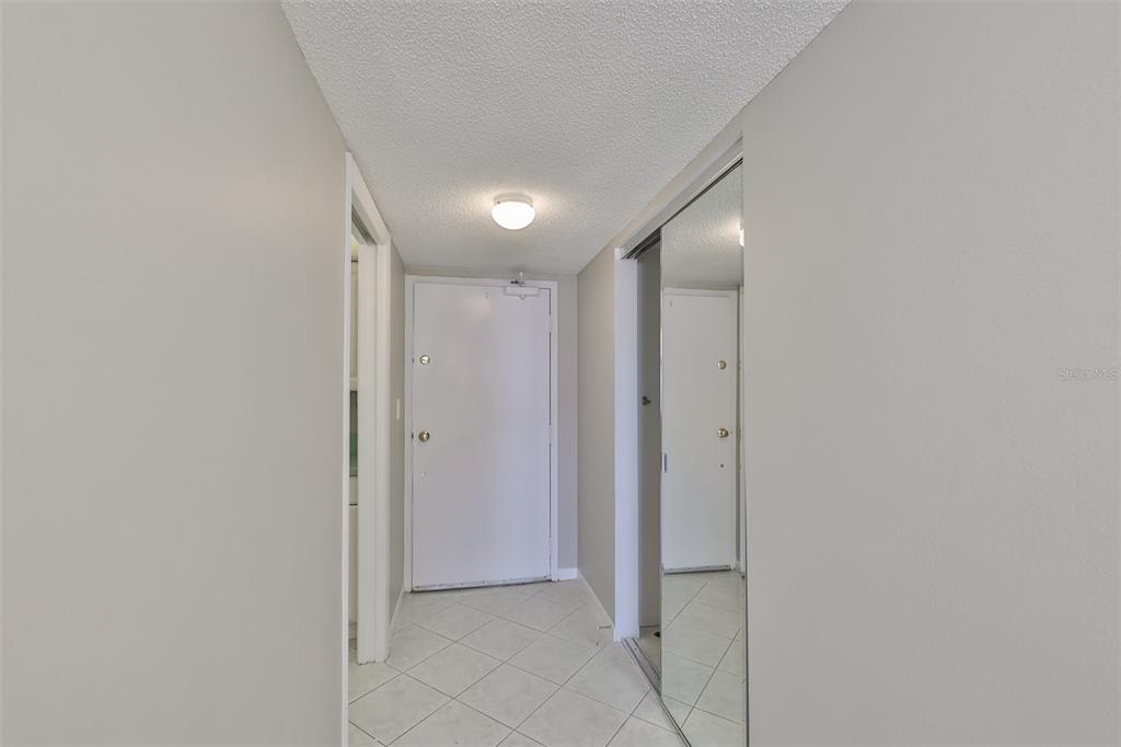 A hallway with white tile flooring, a white door, and a mirrored closet door — 1270 GULF BOULEVARD UNIT 1706, CLEARWATER BEACH, FL