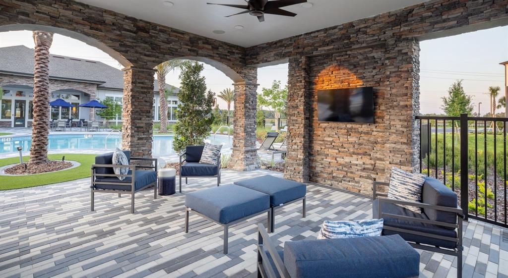 A covered outdoor patio features stone pillars, a wall-mounted television, and modern blue lounge furniture — 3110 GOWAN DRIVE UNIT A1, WINTER HAVEN, FL