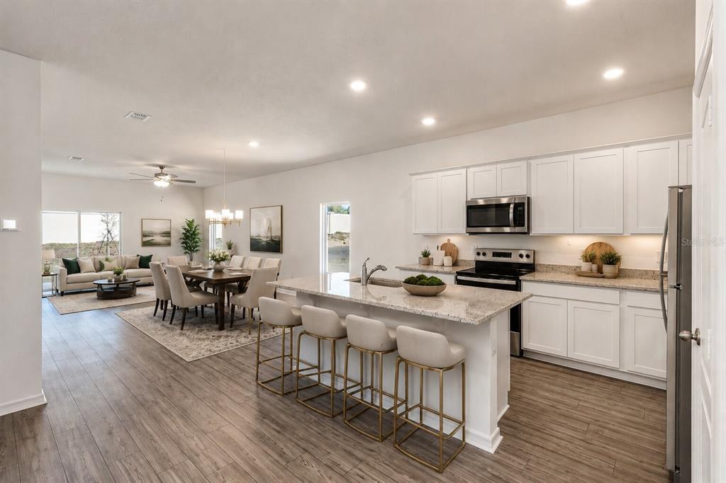 An open-concept kitchen and dining area featuring white cabinetry, granite countertops, and wood-look flooring — 1782 WHITE ELEPHANT, WINTER HAVEN, FL