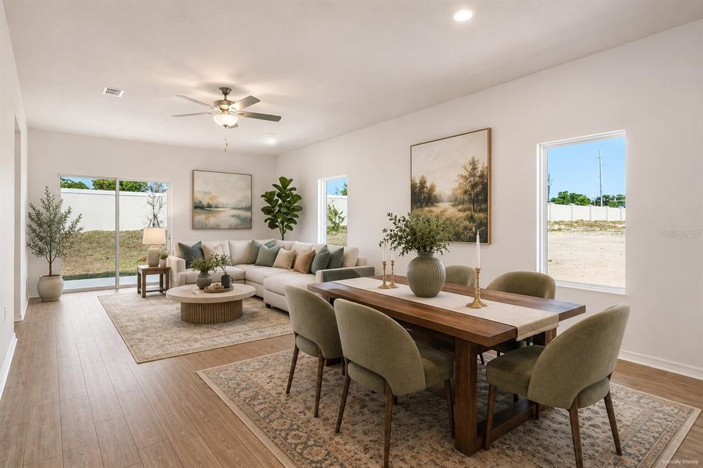 An open-concept living and dining room with light wood floors, neutral furniture, and large windows — 1782 WHITE ELEPHANT, WINTER HAVEN, FL