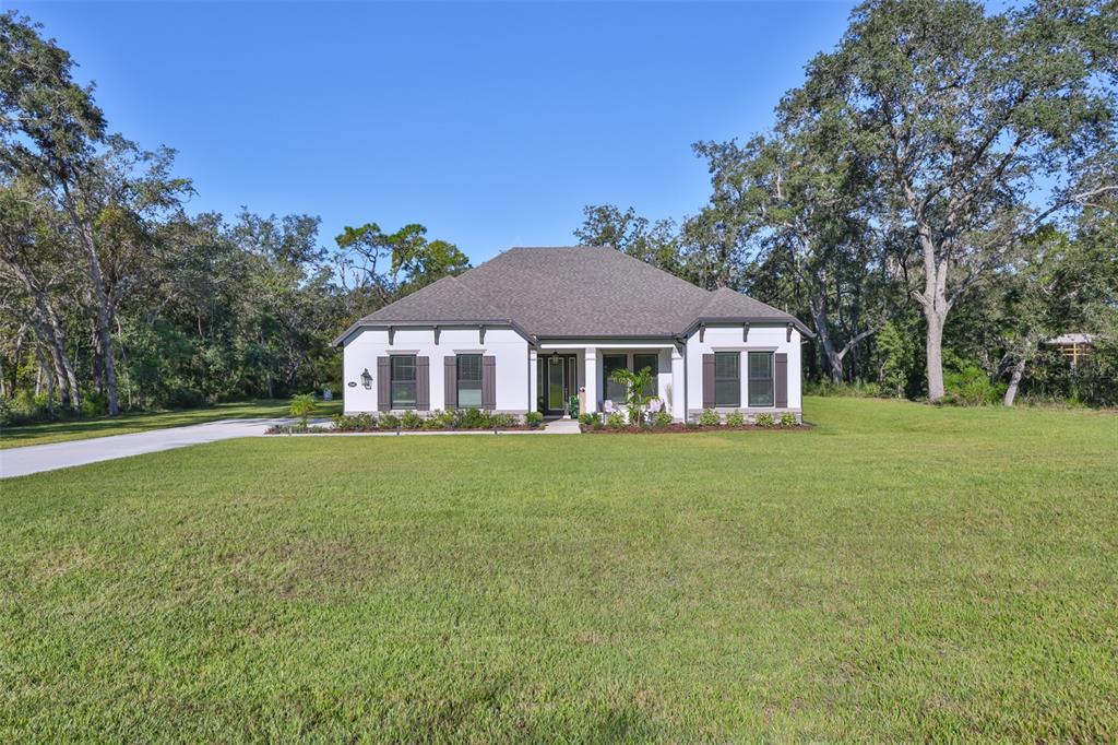 A single-story white house with dark shutters sits on a large, grassy lawn — 13148 OLDENBURG DRIVE, HUDSON, FL