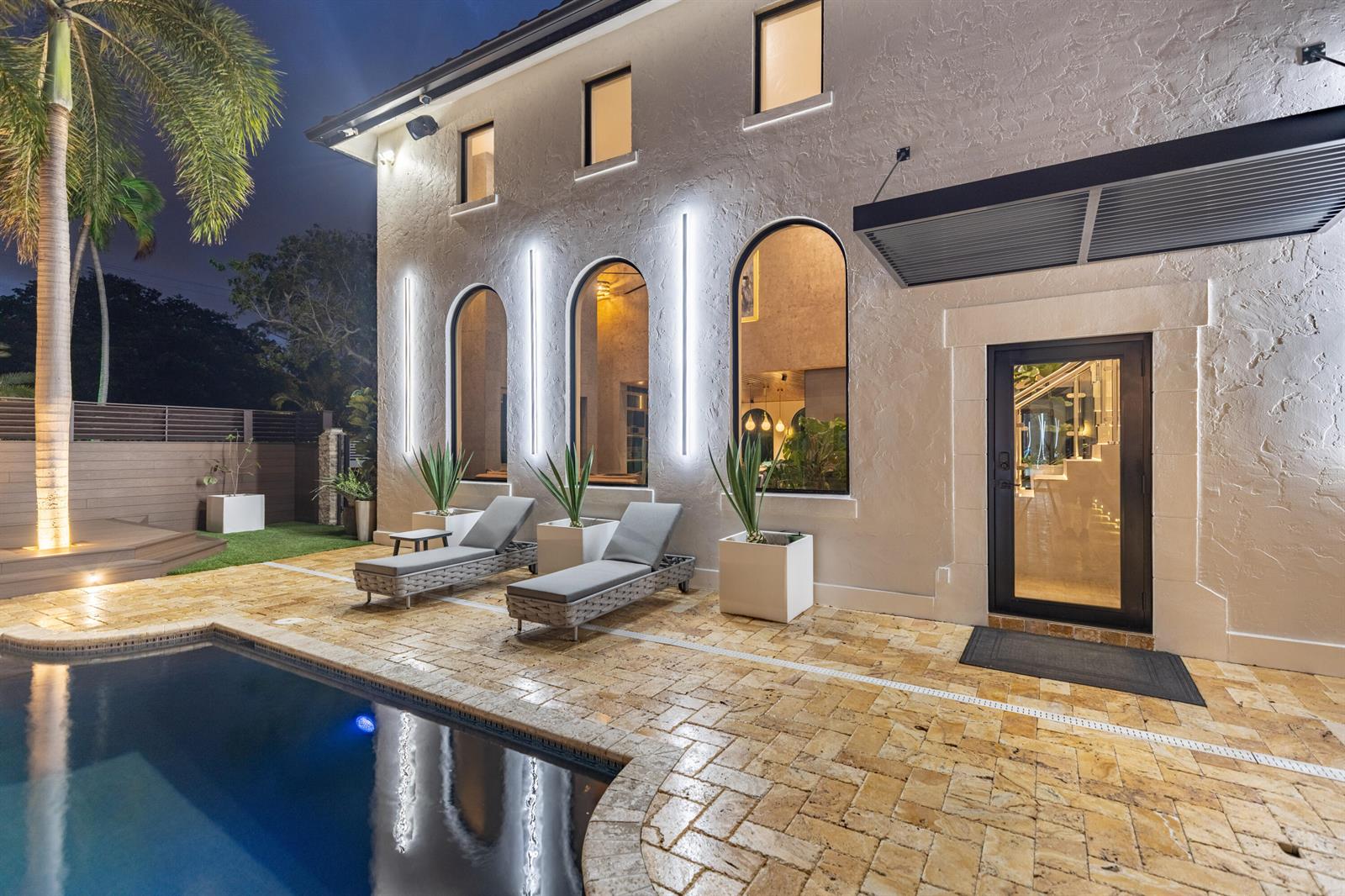 An exterior view of a house at night featuring a pool, lounge chairs, and lighting — 290 NW 6th Street, Boca Raton FL 33432, BOCA RATON, FL