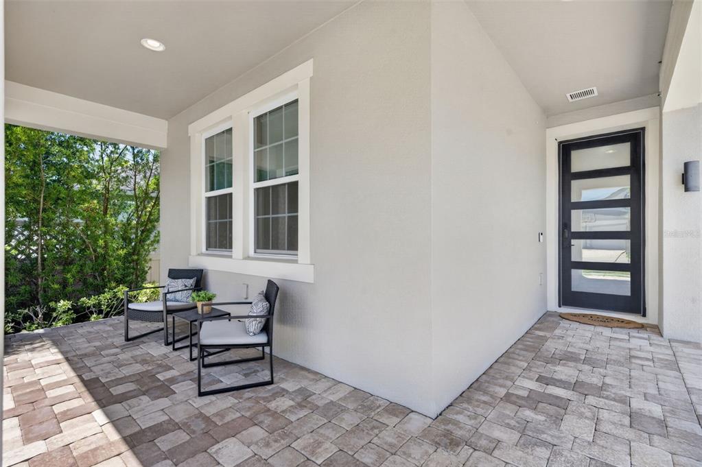 A covered patio features paver flooring, two chairs with a small table, and a front door — 9202 MERLON DRIVE, WINTER GARDEN, FL