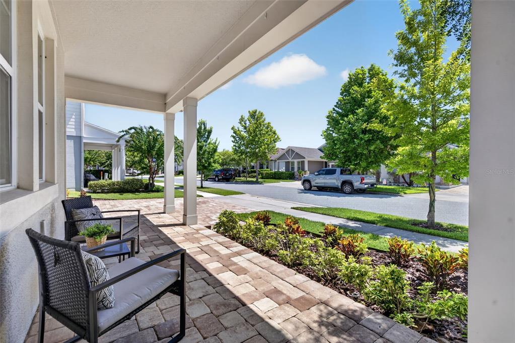 A covered front porch with stone pavers, two chairs, and a view of the street — 9202 MERLON DRIVE, WINTER GARDEN, FL