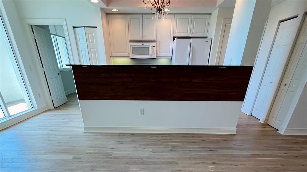 A kitchen features white cabinets, a dark wood-paneled breakfast bar, and light wood flooring — 800 N TAMIAMI TRAIL UNIT 205, SARASOTA, FL
