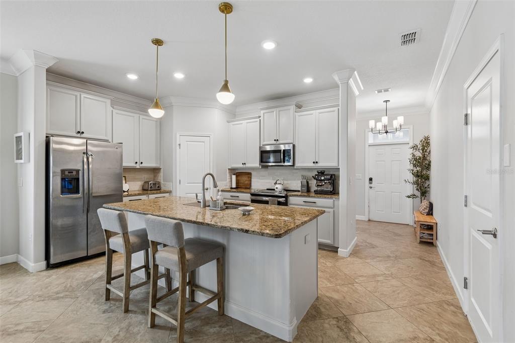 A kitchen features white cabinetry, granite countertops, a central island with bar stools, and tile flooring — 13170 GREEN VIOLET DRIVE, RIVERVIEW, FL