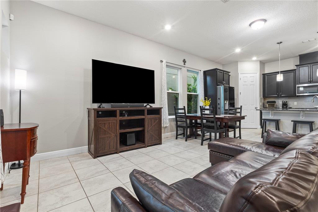 A living room with tile floors, a dark leather sectional, and an open kitchen area — 14536 GOLDEN HARBOR LANE, WINTER GARDEN, FL