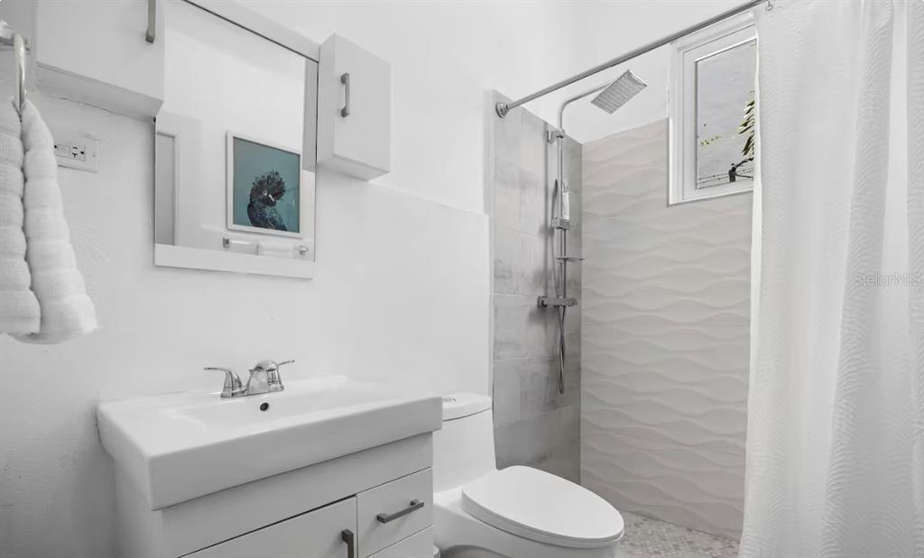 A bathroom features a white vanity, a toilet, and a walk-in shower with textured tiles — 250 CALLE DEL PARQUE UNIT 1B, SAN JUAN, PR