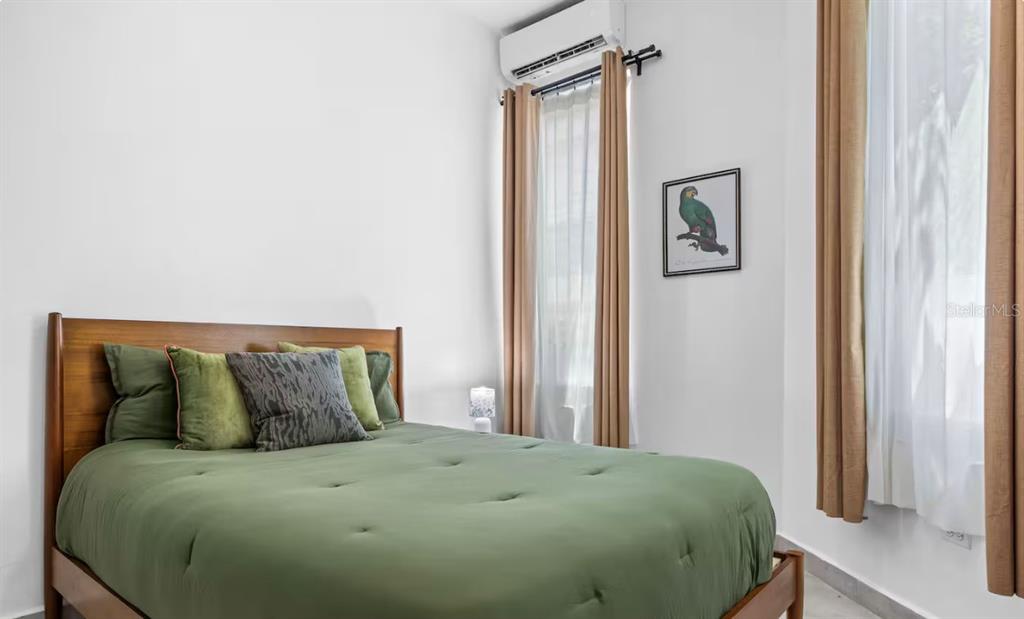 A bedroom features a bed with a green comforter, two windows with curtains, and artwork — 250 CALLE DEL PARQUE UNIT 1B, SAN JUAN, PR