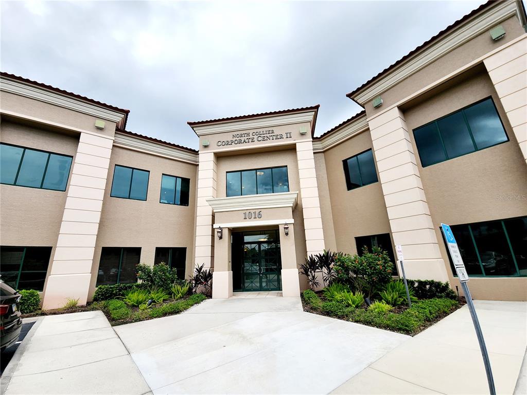 The exterior of a two-story commercial building features a tan facade with dark-tinted windows — 1016 COLLIER CENTER WAY UNIT 106, NAPLES, FL