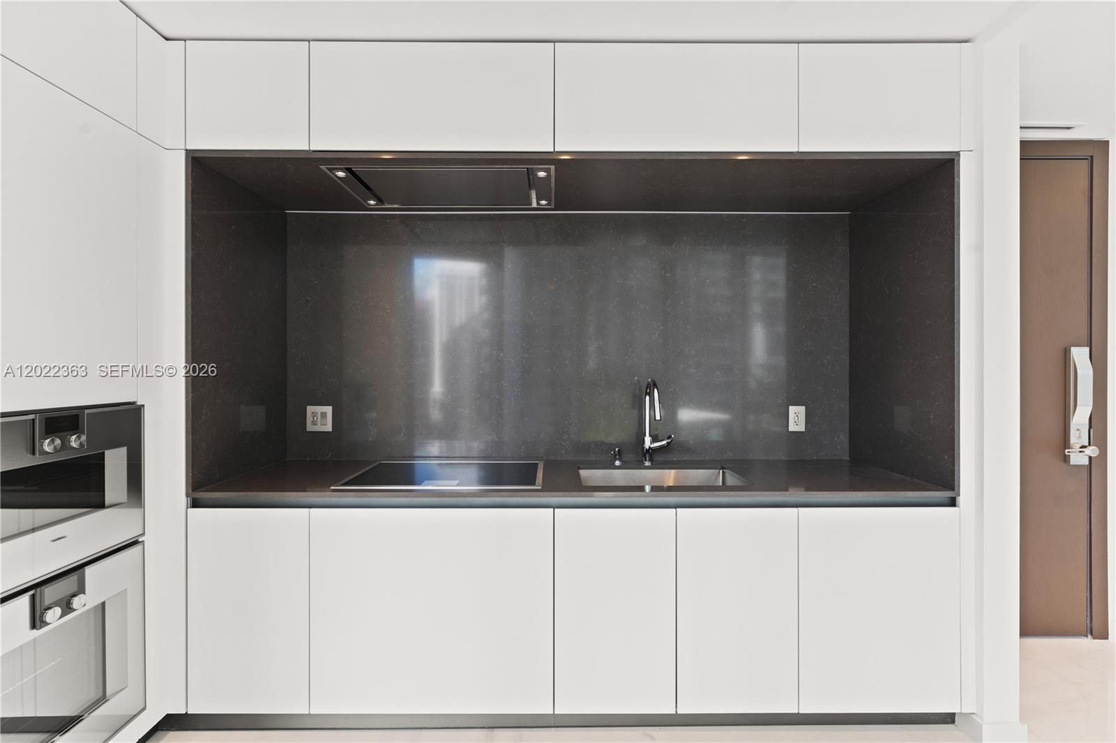 A modern kitchen features white cabinets, a dark stone backsplash, a cooktop, and a sink — 300 Biscayne Blvd Way # 1406, Miami FL 33131, MIAMI, FL