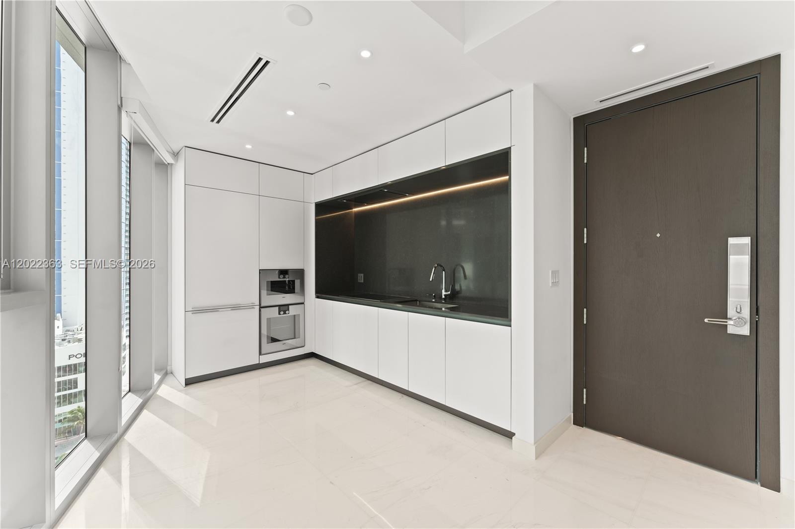 A modern kitchen features white cabinetry, dark countertops, built-in appliances, and floor-to-ceiling windows — 300 Biscayne Blvd Way # 1406, Miami FL 33131, MIAMI, FL