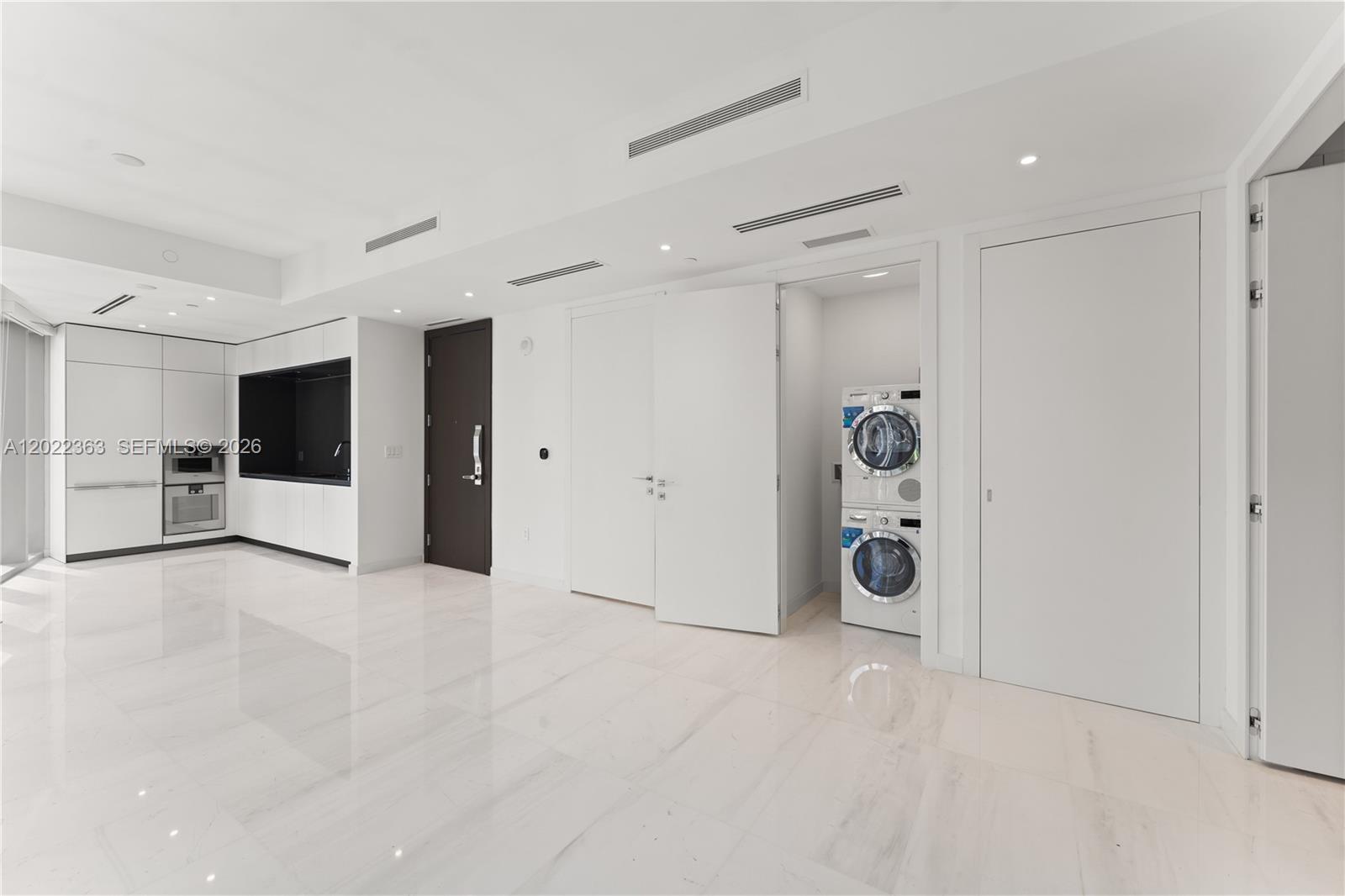 A modern, minimalist room features white tile floors, white cabinetry, and a stacked laundry unit — 300 Biscayne Blvd Way # 1406, Miami FL 33131, MIAMI, FL