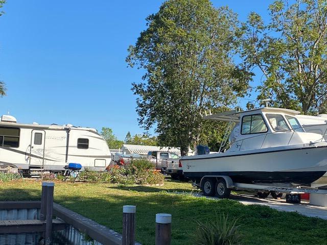 A white travel trailer and a motorboat on a trailer sit on a grassy lot — 8680 Us Highway 441 SE, Okeechobee FL 34974, OKEECHOBEE, FL