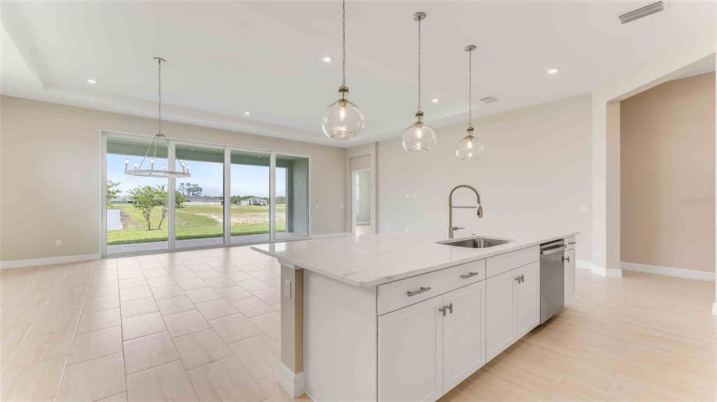 A modern kitchen with a white island and pendant lights overlooks a spacious living area — 1017 LILIANA DRIVE, DELAND, FL