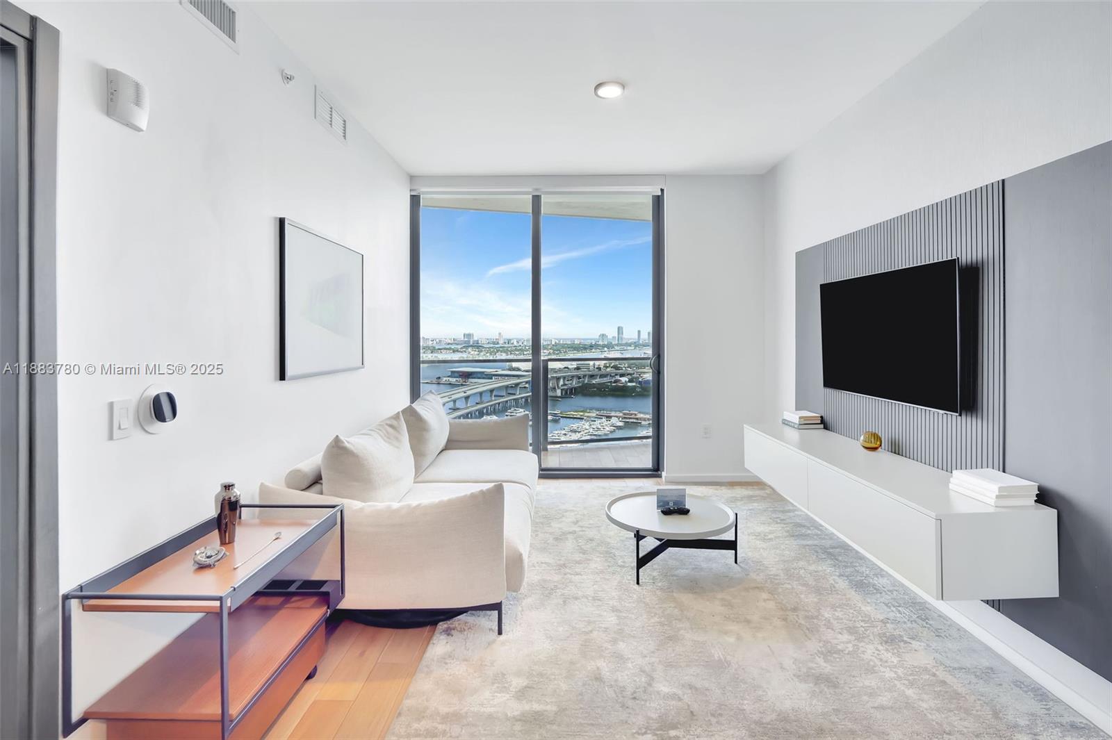 A modern living room features a white sofa, wall-mounted television, and a balcony with water views — 398 NE 5th St # 1910, Miami FL 33132, MIAMI, FL
