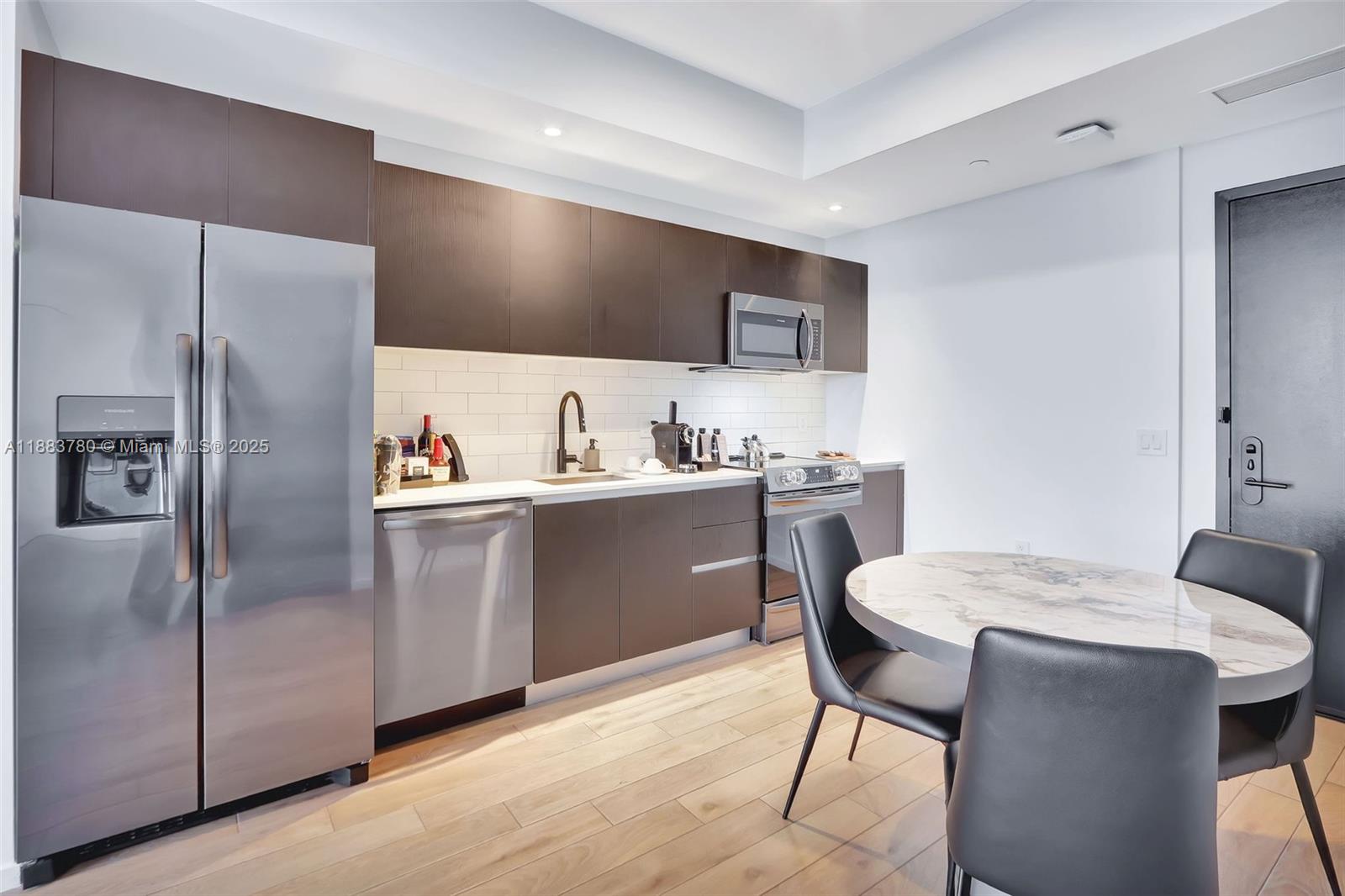 A modern kitchen features dark wood cabinetry, stainless steel appliances, and a small dining table — 398 NE 5th St # 1910, Miami FL 33132, MIAMI, FL