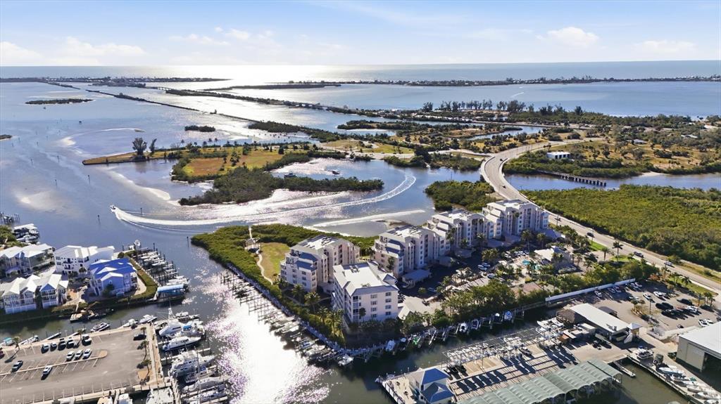 An aerial view shows waterfront condominium buildings, a marina, and a bridge over the bay — 13113 GASPARILLA ROAD UNIT 403, PLACIDA, FL