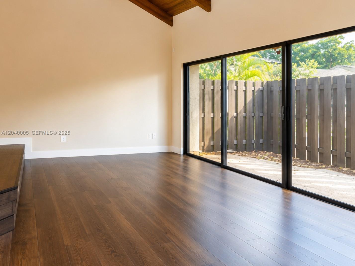 An empty room features dark wood flooring, beige walls, vaulted ceilings, and large sliding glass doors — 8021 SW 21st Ct, Davie FL 33324, DAVIE, FL