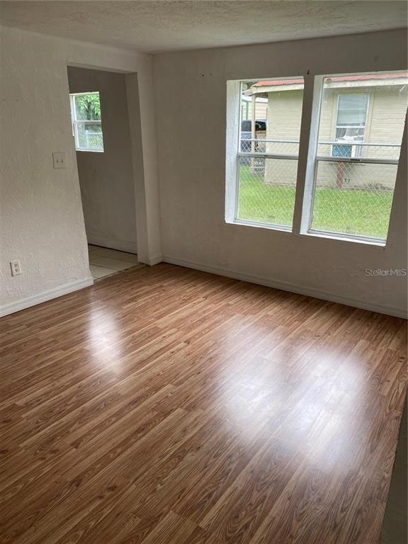 An empty room with wood-look laminate flooring, white walls, and two windows overlooking a yard — 414 NW 9TH AVENUE, OCALA, FL