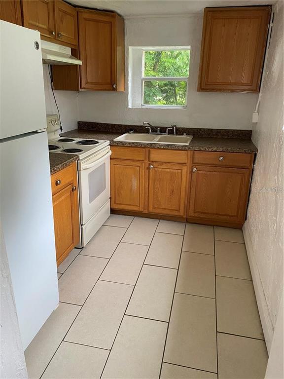 A kitchen features wooden cabinets, a white stove, a double sink, and light-colored floor tiles — 414 NW 9TH AVENUE, OCALA, FL